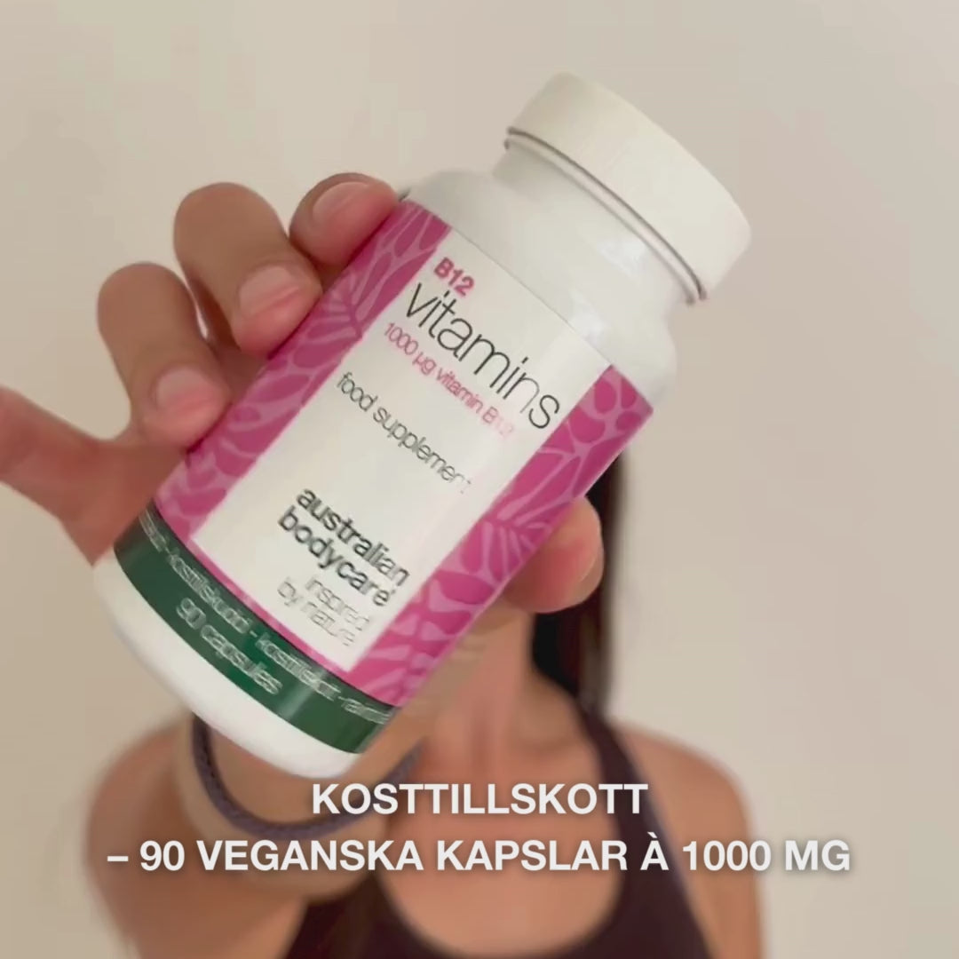 Närbild av en hand som håller Vitamin B12 kosttillskott, öppnar locket och häller ut släta, vita kapslar—visar produkten för dagligt bruk för energi, immunförsvar, nervsystem och minskad trötthet.