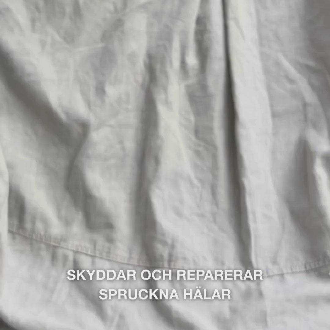 Närbild av en hand som tar en rik, krämig mängd Heel Repair i handflatan och varsamt masserar in den i torr, sprucken hälhud: den tjocka konsistensen absorberas synligt, mjukar upp och återfuktar, medan 25 % urea, sheasmör och tea tree-olja lugnar och skyddar huden.