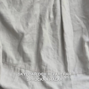 Närbild av en hand som tar en rik, krämig mängd Heel Repair i handflatan och varsamt masserar in den i torr, sprucken hälhud: den tjocka konsistensen absorberas synligt, mjukar upp och återfuktar, medan 25 % urea, sheasmör och tea tree-olja lugnar och skyddar huden.