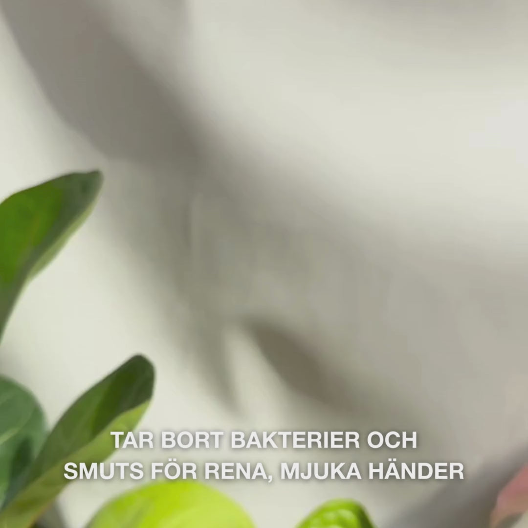 Närbild av händer som pumpar klar, ljusblå, skummande flytande handtvål med Tea Tree Oil i handflatan och varsamt skummar den över handflator, handryggar och mellan fingrarna — den lena, rengörande skummet tar bort bakterier och smuts samtidigt som den mjukgör och återfuktar huden.