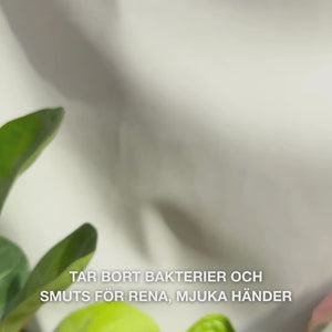 Närbild av händer som pumpar klar, ljusblå, skummande flytande handtvål med Tea Tree Oil i handflatan och varsamt skummar den över handflator, handryggar och mellan fingrarna — den lena, rengörande skummet tar bort bakterier och smuts samtidigt som den mjukgör och återfuktar huden.